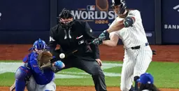 Yankees batter hitting the ball during the 2024 World Series against opposing catcher and umpire.