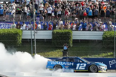 NASCAR driver performing a burnout in the No. 12 Wabash car in front of cheering fans at the Pocono Raceway during the Great American Getaway 400